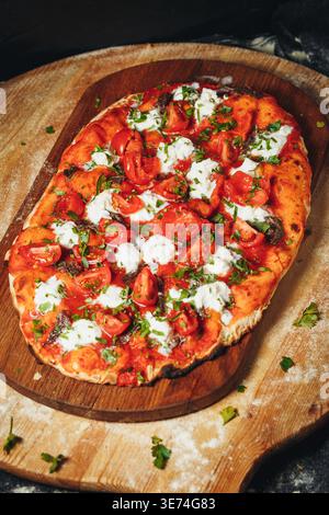 Pinsa romana italienne traditionnelle garnie de sauce tomate fraîche, de fromage mozzarella crémeux et de tomates cerises juteuses sur une planche de bois rustique. Banque D'Images