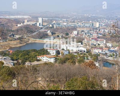 Une vue panoramique surélevée depuis une colline boisée surplombant une ville de banlieue avec un réservoir ou un lac, des bâtiments résidentiels et des montagnes lointaines Banque D'Images