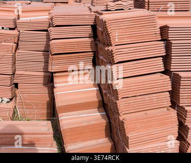 Grandes piles soigneusement empilées de tuiles de toit en terre cuite rouges prêtes à être installées à l'extérieur. La scène représente les matériaux de construction, la construction industr Banque D'Images