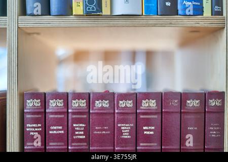 Photographie en gros plan d'une étagère en bois présentant deux étagères de livres. L'étagère inférieure comporte une rangée uniforme de livres reliés de couleur bordeaux Banque D'Images