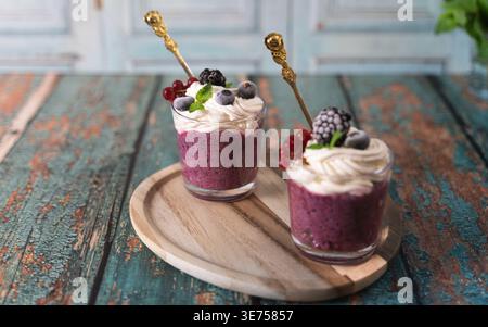 Composition de deux desserts aux baies avec de la crème et des fruits sur planche de bois sur fond rustique. Banque D'Images