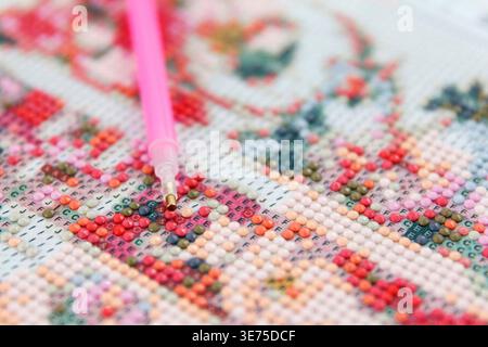 Gros plan d'une peinture de diamant colorée en cours. Un applicateur rose est utilisé pour placer des pierres précieuses étincelantes sur un motif floral Banque D'Images