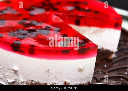 Un gros plan de cheesecake garni de gelée rouge et de baies noires. La croûte est à base de chocolat, et le dessert est servi sur un plateau foncé Banque D'Images