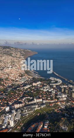 Vue aérienne de Funchal, Madère, montre baie en croissant, port de plaisance, long quai de croisière, collines escarpées, falaises de Cabo Girao, lune dans le ciel profond, et hiver comme c Banque D'Images