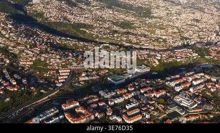 Vue aérienne de Funchal, Madère, montre des toits en terrasses, des ravins, un échangeur routier et un long viaduc, et un complexe moderne avec cour sur le toit en lat Banque D'Images