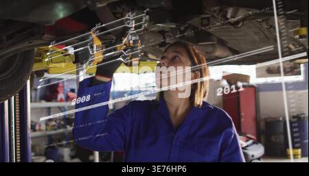 Inspecter le mécanicien en vérifiant sous la voiture sur l'ascenseur dans le garage avec des gants de combinaison et le recouvrement AR Banque D'Images