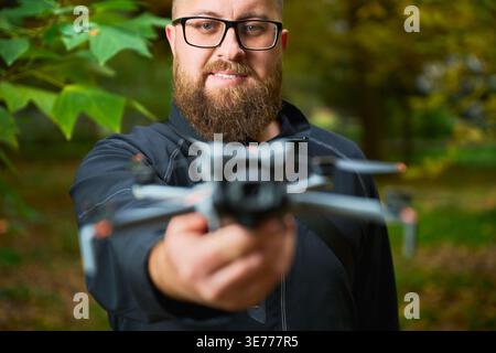 L'homme tient le drone vers le dispositif d'affichage de caméra. Homme barbu présentant quadcopter dans le parc avec une faible profondeur de champ, se concentrer sur la technologie et le design, concept de technologie moderne et passe-temps Banque D'Images