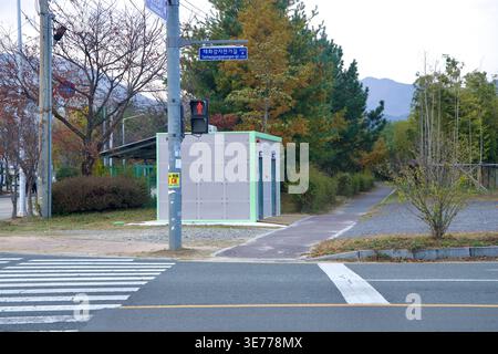 Une petite entrée de chemin et un croisement se trouvent à côté du sentier Taehwagang à Ulju-gun, avec une structure utilitaire, des arbres en bordure de route, des bambous et des sig de rue locale Banque D'Images
