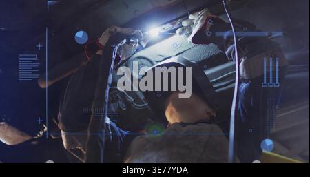 Réparation femme mécanicien portant casque et combinaisons sombres sous le véhicule au garage, tenant la torche Banque D'Images