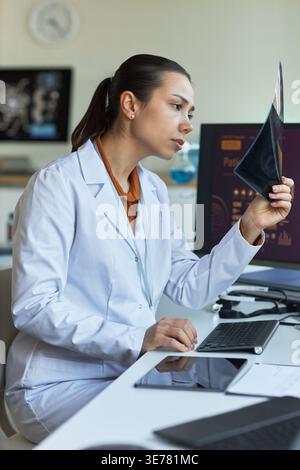 Plan vertical d'une jeune femme asiatique examinant un film radiographique au poste de travail et examinant les résultats du diagnostic. Adapté au marketing des soins de santé, aux services de radiologie et à la technologie médicale Banque D'Images