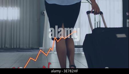 Femme qui marche portant une jupe tirant une valise noire dans le hall de l'hôtel avec des graphiques oranges et rouges Banque D'Images