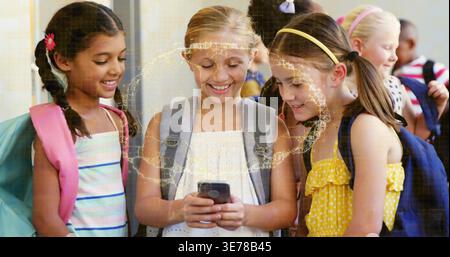 Se blottissant trois filles en regardant leur smartphone dans le couloir de l'école, portant des sacs à dos et des vêtements d'été Banque D'Images