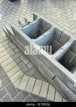 Une vue rapprochée de blocs de béton creux assemblés sur un patio pavé à motifs, suggérant un projet de construction ou d’aménagement paysager en cours Banque D'Images