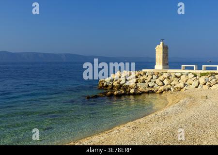 Petit phare sur la jetée rocheuse avec mer Adriatique claire. Point de repère côtier en Croatie Banque D'Images