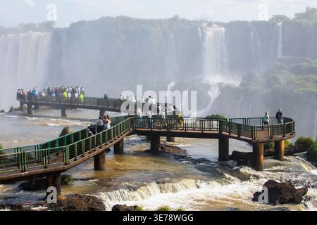Des dizaines de touristes se rassemblent sur les passerelles métalliques surélevées qui s'étendent sur les eaux turbulentes des chutes d'Iguazu, l'une des plus grandes et des plus spectacu du monde Banque D'Images