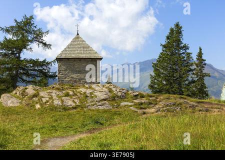 Petite chapelle en pierre sur une colline dans les Alpes autrichiennes près de Grossglockner avec paysage de montagne et arbres. Paysage alpin paisible. Banque D'Images