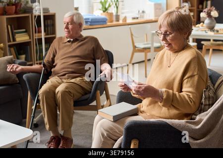 Femme caucasienne senior regardant des photos alors que l'homme caucasien senior reçoit une perfusion IV à proximité, soutenant les soins de santé et le marketing des soins aux personnes âgées Banque D'Images