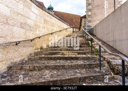 D'anciennes marches pavées mènent entre des murs de pierre historiques dans la ville médiévale de Porrentruy, en Suisse, avec des mains courantes modernes en métal pour s. Banque D'Images