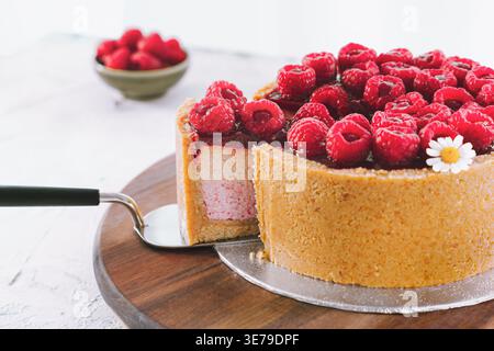 Tranche de gâteau aux framboises servi avec des baies fraîches sur planche de bois dans une cuisine lumineuse, dessert servant, cuisson maison Banque D'Images