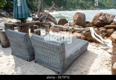 Chaises longues dans un bar rustique sur l'île de la Digue, aux Seychelles, face aux rochers de granit, au sable blanc et aux eaux bleues limpides de l'océan Indien, surrou Banque D'Images
