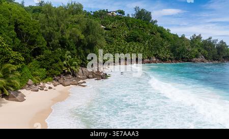 Une plage tropicale isolée avec de grands rochers et des palmiers luxuriants, des eaux turquoises baignant le rivage. Anse intendance. Seychelles, Mahé. Banque D'Images