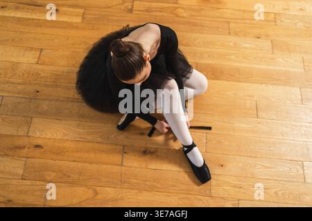 Ballerina met sur les chaussures de pointe sur la jambe en classe de danse. Danseuse de ballet classique dans le studio de danse. Ballerine mettant sur attacher des chaussures de pointe classiques pour l'entraînement de danse. Concept d'école de ballet Banque D'Images