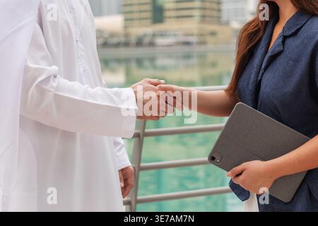Femme asiatique et client émirati se serrent la main à Dubai Marina tout en discutant d'un accord d'investissement immobilier avec intérêt mutuel. Banque D'Images