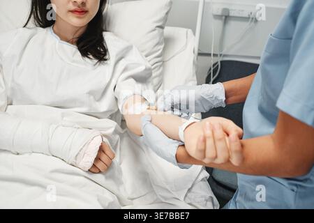 Infirmier du moyen-Orient recevant une thérapie intraveineuse chez une patiente asiatique allongée au lit dans une chambre d'hôpital Banque D'Images