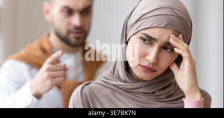 Femme musulmane arabe déprimée en hijab touchant sa tête alors qu'elle se faisait crier dessus par son mari caucasien à la maison Banque D'Images