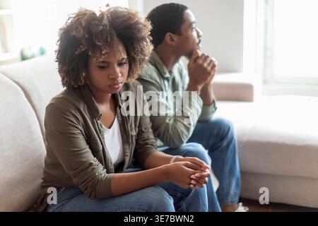 Conflit familial. Triste couple africain assis sur le canapé dos à dos éviter de parler après le combat, homme offensé et femme séparés sur le canapé ignorant l'un l'autre, Banque D'Images