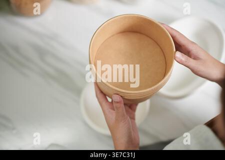 Mains de femme asiatique tenant bol tout en se tenant debout dans la cuisine à la maison Banque D'Images