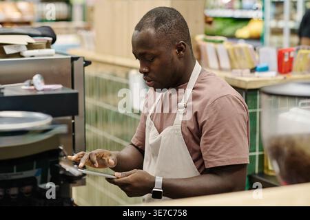 Commis de magasin mâle noir utilisant la tablette debout dans l'épicerie Banque D'Images