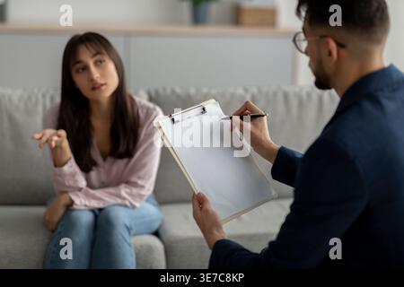 Femme du moyen-Orient parlant à un psychologue masculin tout en étant assis sur le canapé pendant la séance de thérapie en clinique Banque D'Images