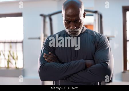 Homme afro-américain senior en haut athlétique sombre, bras croisés debout, réfléchissant par rack de puissance Banque D'Images