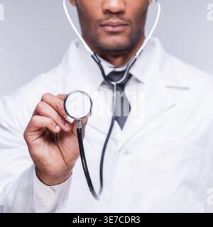 Docteur noir portant et montrant le stéthoscope tout en se tenant debout sur fond gris en studio Banque D'Images