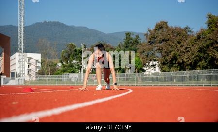Coureuse féminine thaïlandaise en position de départ accroupie prête à courir sur la piste dans le stade le jour ensoleillé Banque D'Images