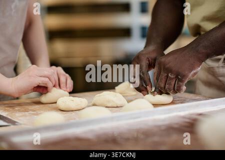 Mains mâles noires et femelles caucasiennes préparant des petits pains dans la cuisine de boulangerie Banque D'Images