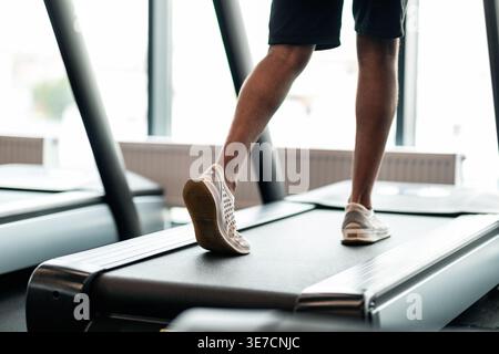 Image recadrée de Black Man jogging sur tapis roulant dans le gymnase Banque D'Images