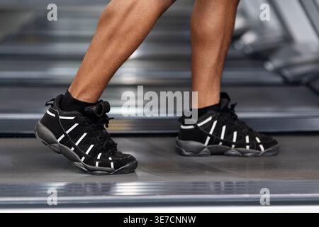 Image recadrée d'un homme noir s'entraînant sur un tapis roulant debout dans la salle de gym pendant l'entraînement Banque D'Images