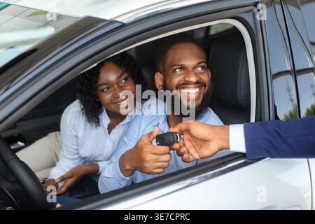 Couple noir prenant les clés de voiture du vendeur tout en étant assis dans la voiture à la salle d'exposition Banque D'Images