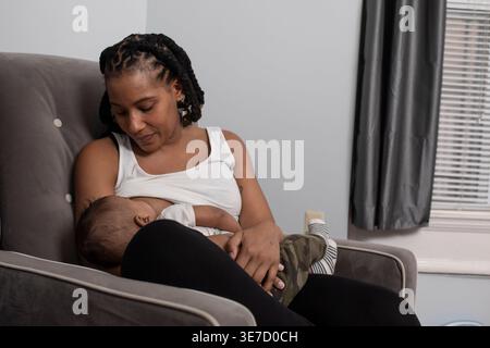 Mère afro-américaine allaitant son nouveau-né garçon tout en étant assise Banque D'Images