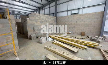 Intérieur de l'entrepôt avec des murs en béton partiellement construits et des matériaux de construction dispersés Banque D'Images