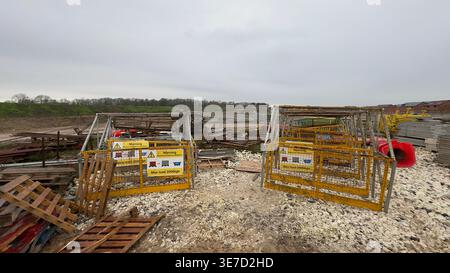 Deux barrières de sécurité jaunes avec des panneaux d'avertissement se dressent sur du gravier sur un chantier de construction avec des palettes empilées et des débris à Taylor Wimpey, Ripon, Royaume-Uni. Banque D'Images