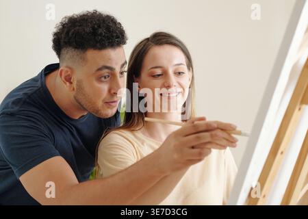 Couple mixte et caucasien se tenant la main tout en peignant sur toile ensemble à la maison Banque D'Images