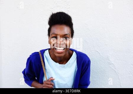 Femme noire souriante penchée en avant avec sac contre mur blanc Banque D'Images