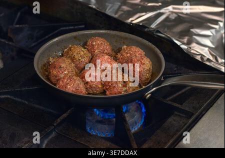 Boulettes de viande cuisant dans une poêle à frire sur une cuisinière à gaz dans la cuisine du restaurant mettant en évidence le processus de cuisson, la chaleur et la préparation des aliments professionnels Banque D'Images