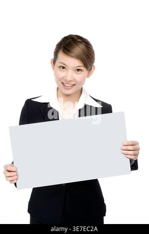 Femme d'affaires chinoise souriante tenant un tableau blanc tout en se tenant debout sur fond blanc dans le studio Banque D'Images