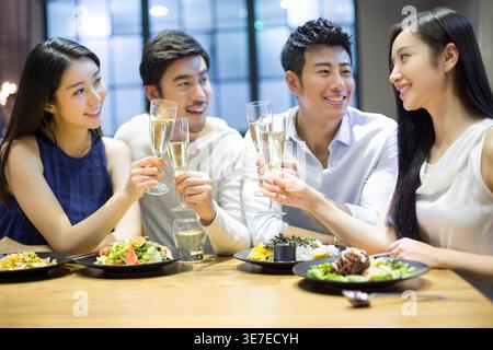 Joyeux amis asiatiques, hommes et femmes, assis à table, à prendre des verres de champagne et à dîner ensemble au restaurant Banque D'Images
