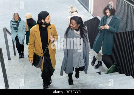 Femme noire souriante et homme caucasien parlant tout en marchant à l'étage aller travailler pendant l'heure de pointe en hiver Banque D'Images