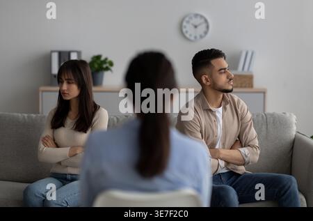 Couple du moyen-Orient regardant loin tout en s'asseyant dos à dos sur le canapé devant la thérapeute féminine en clinique Banque D'Images
